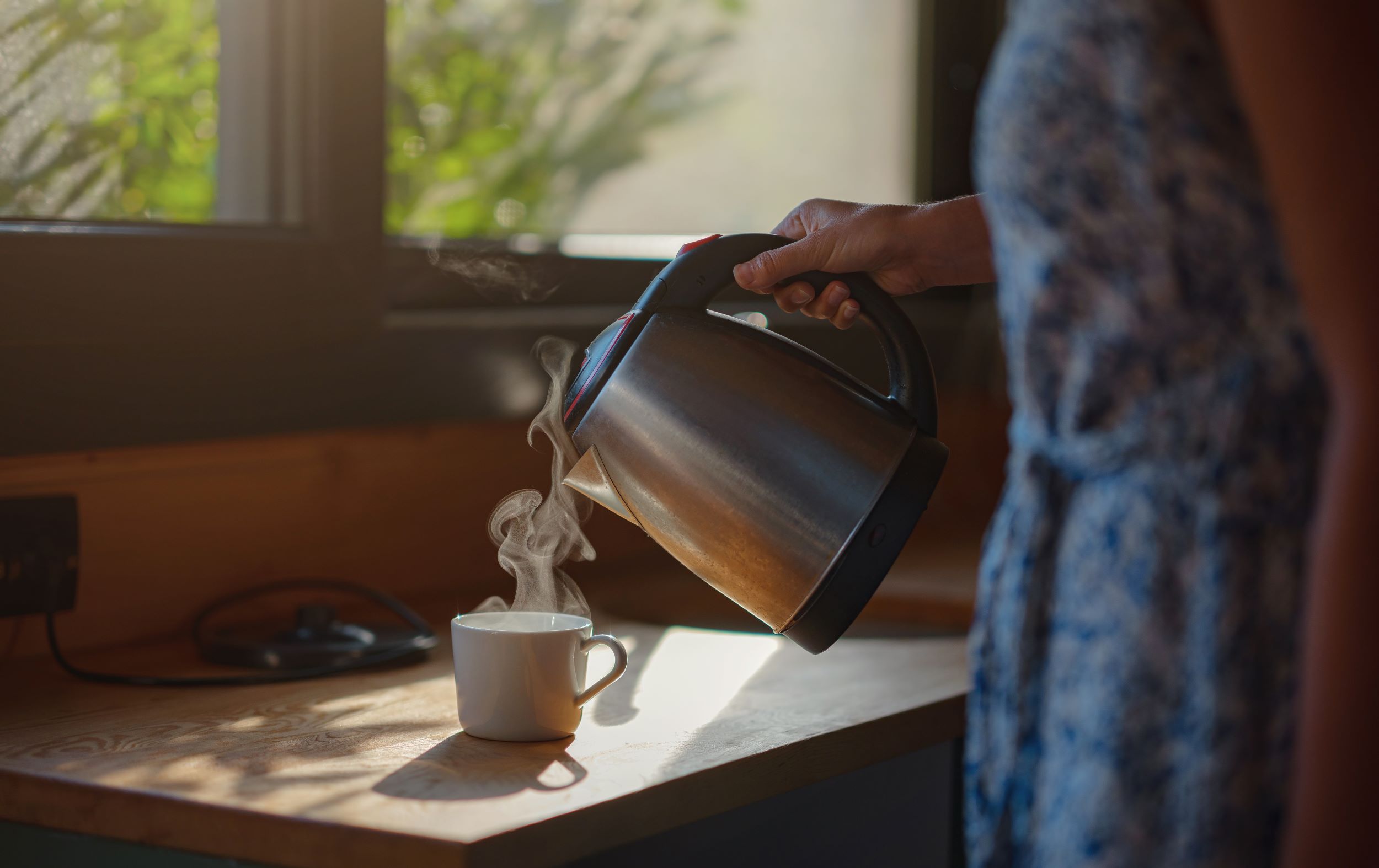 Vrouw schenkt heet water uit waterkoker in een kopje