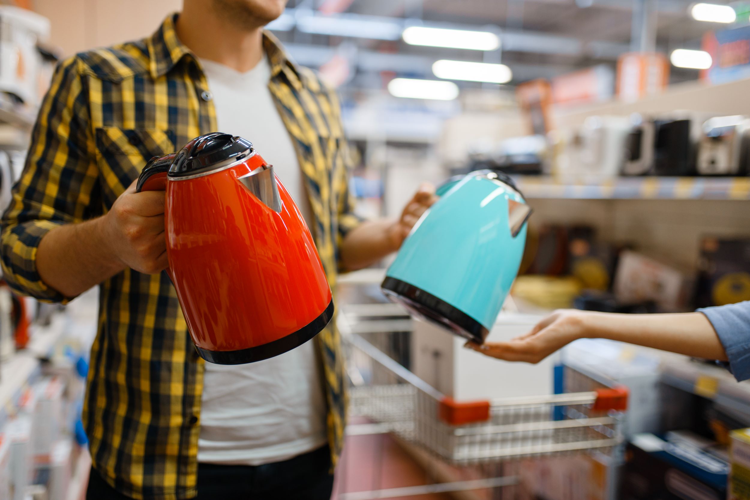 Man staat in een winkel met een rode en een blauwe waterkoker om uit te kiezen