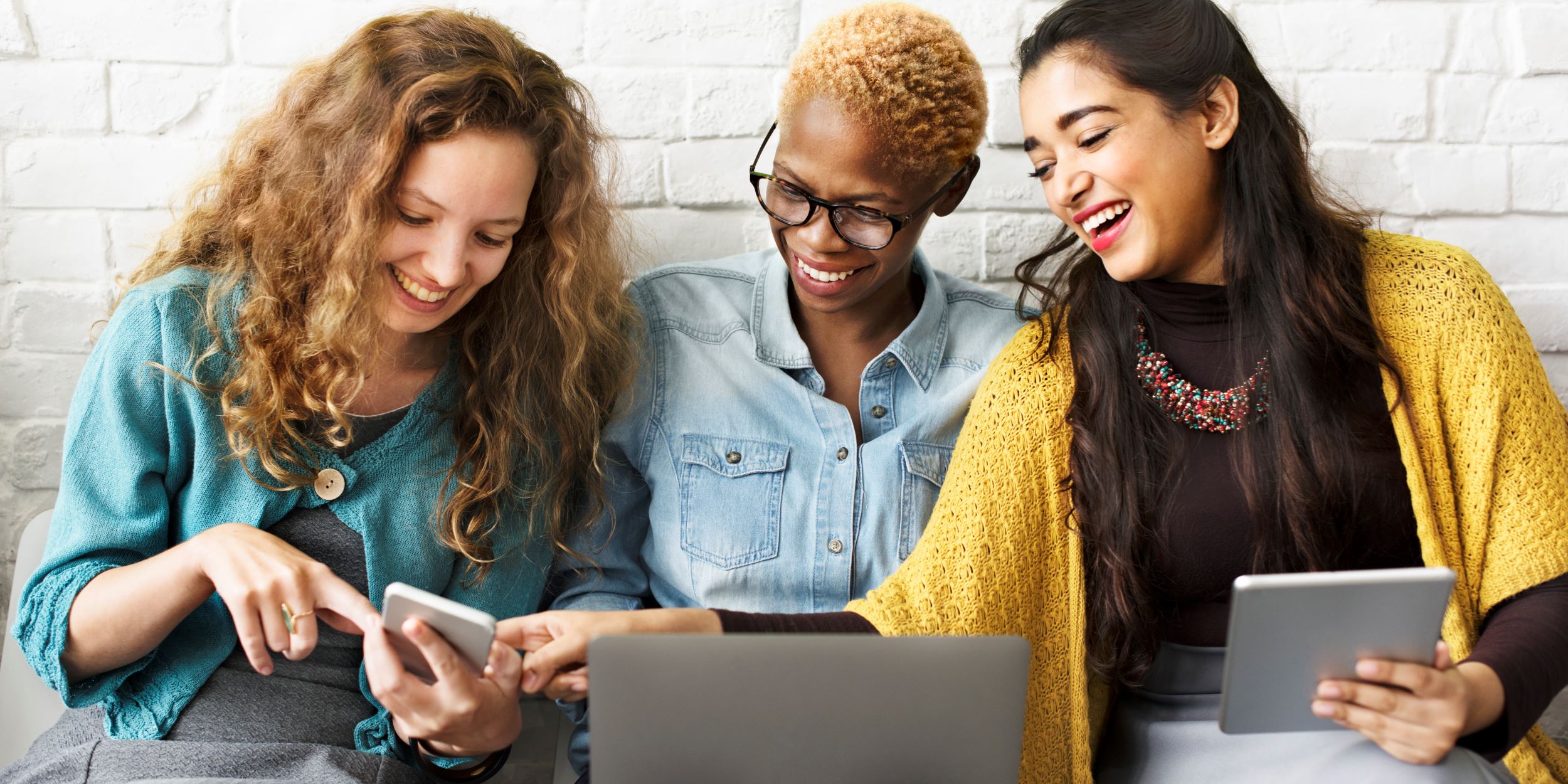 Drie personen die lachen terwijl ze kijken naar een telefoon, laptop en tablet