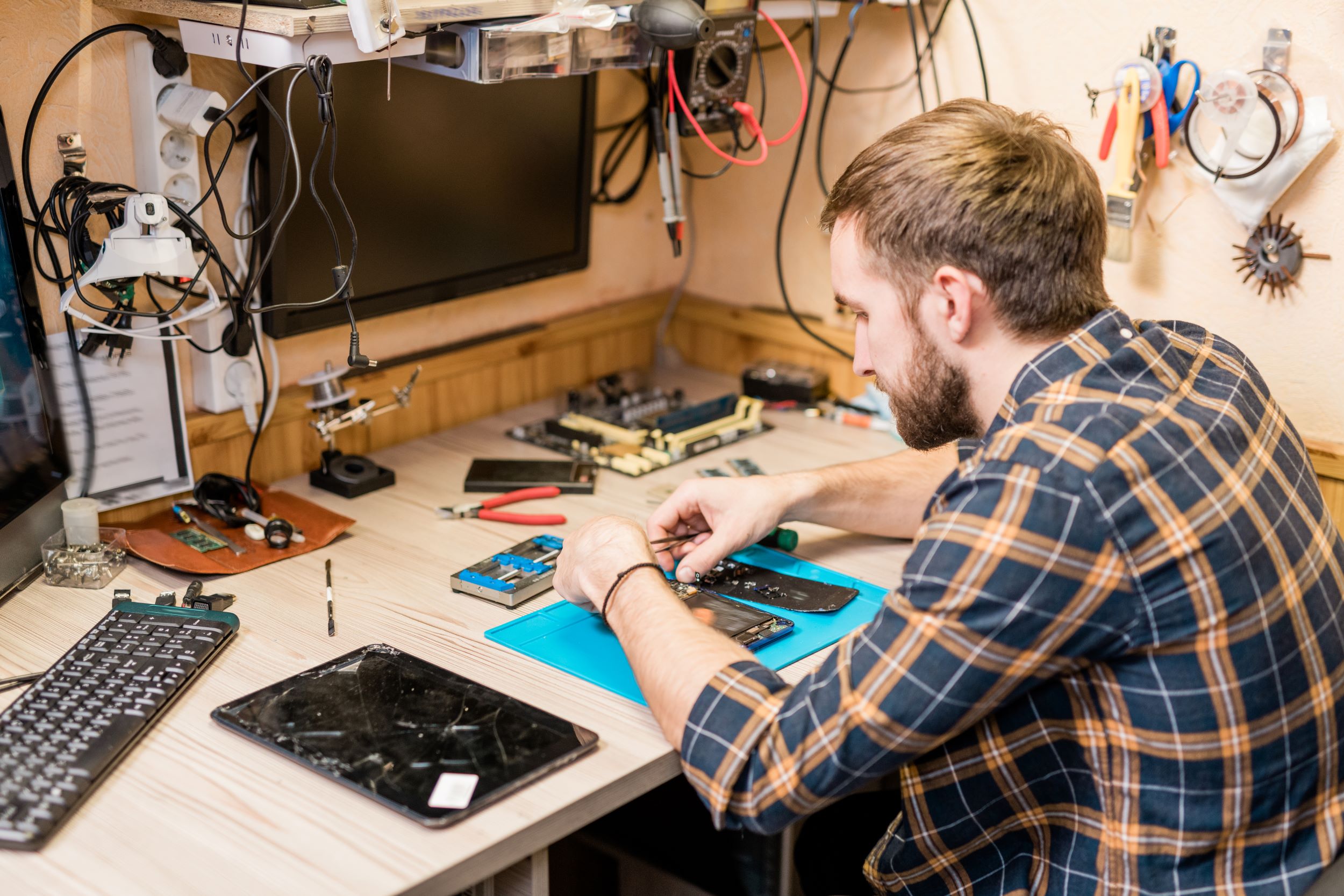 Man met gereedschap om zich heen die een telefoon en tablet repareert