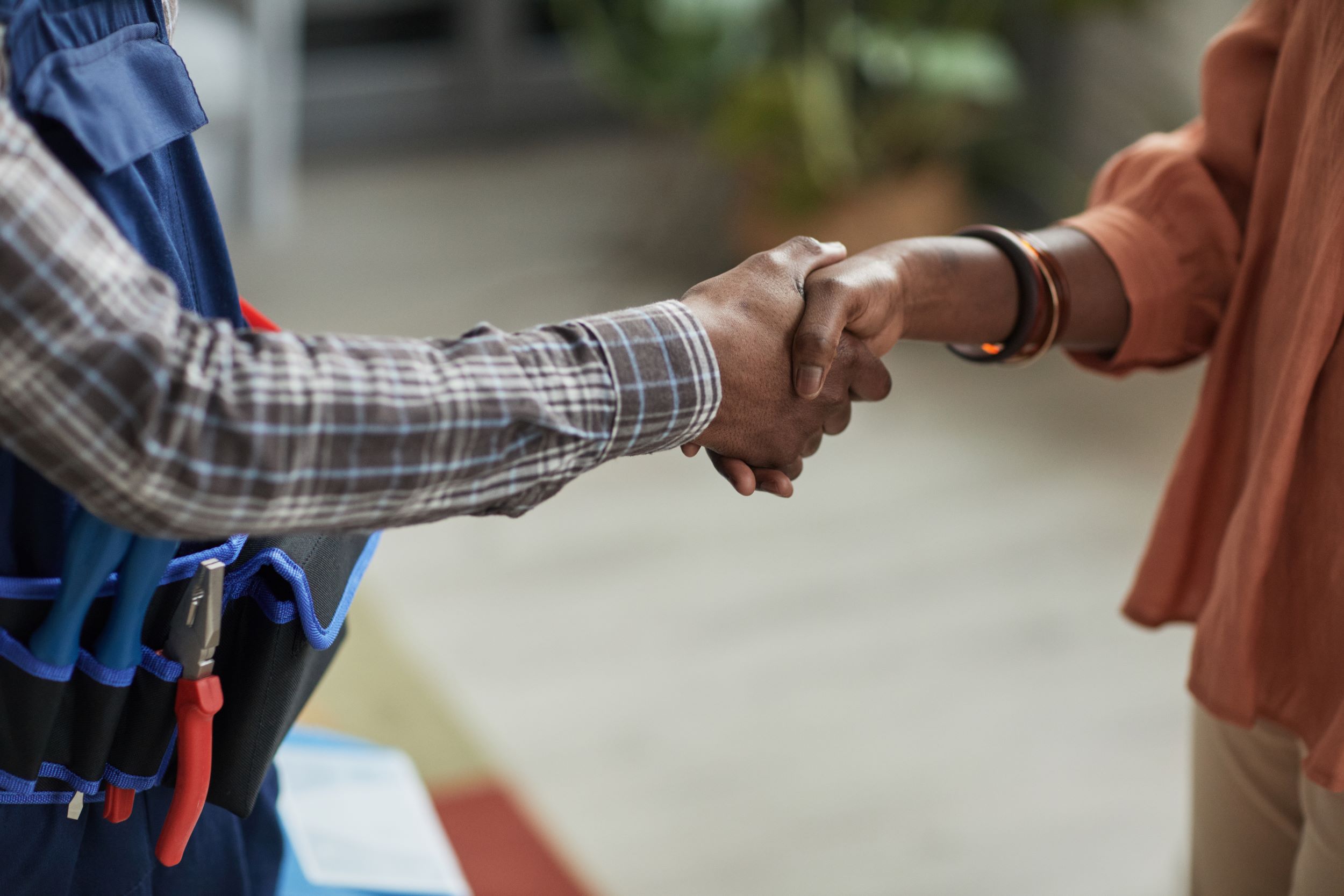 Twee mensen die de hand schudden, een heeft gereedschap om zijn middel