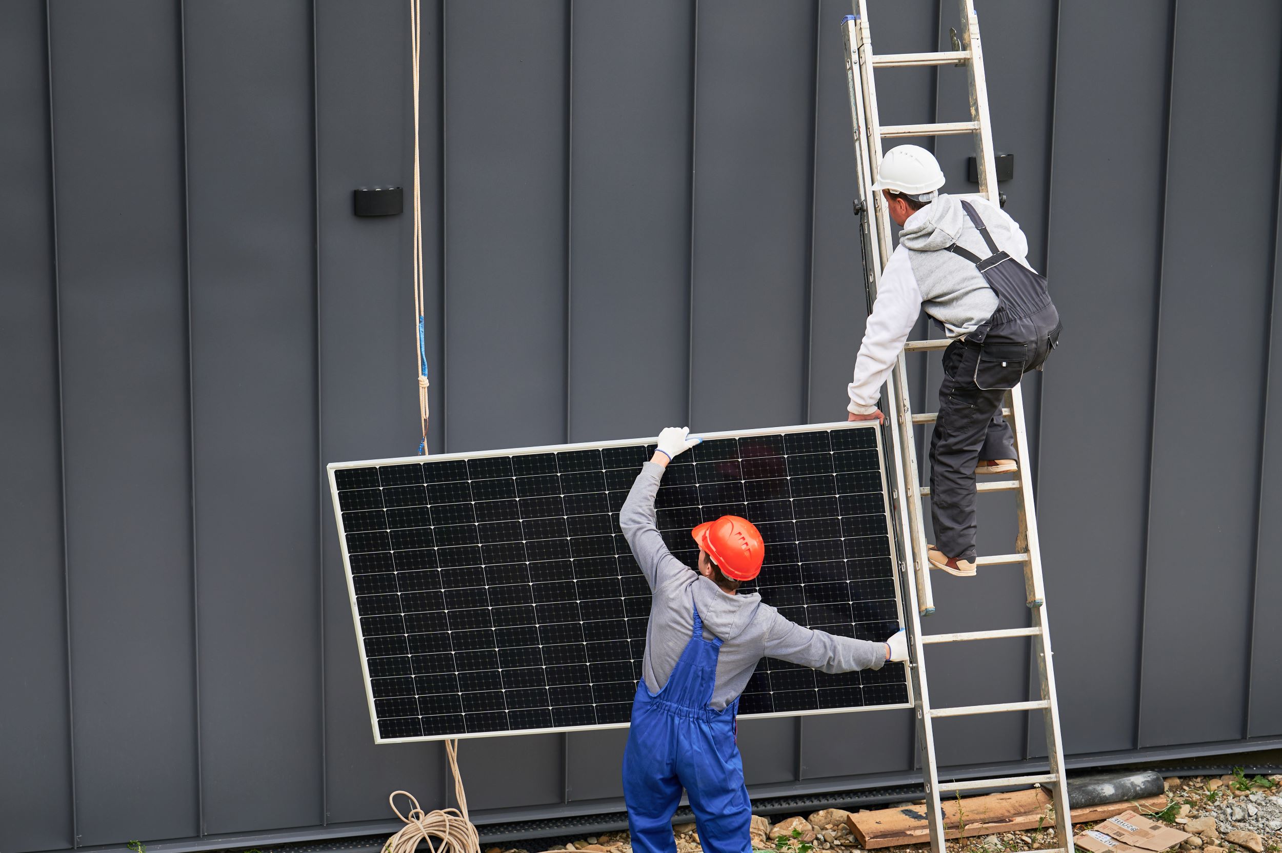 Twee werkers die een zonnepaneel vasthouden, een staat op de grond en de ander op een ladder